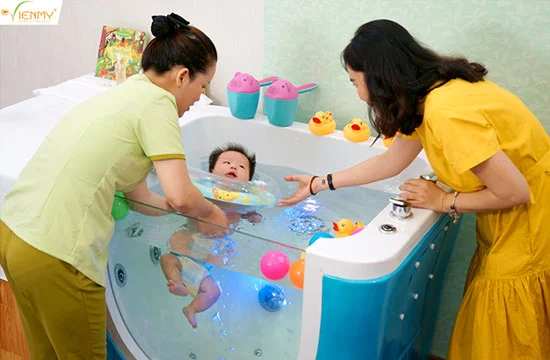 Chuyên viên nhẹ nhàng cho bé tiếp xúc với nước trong bể bơi thủy liệu